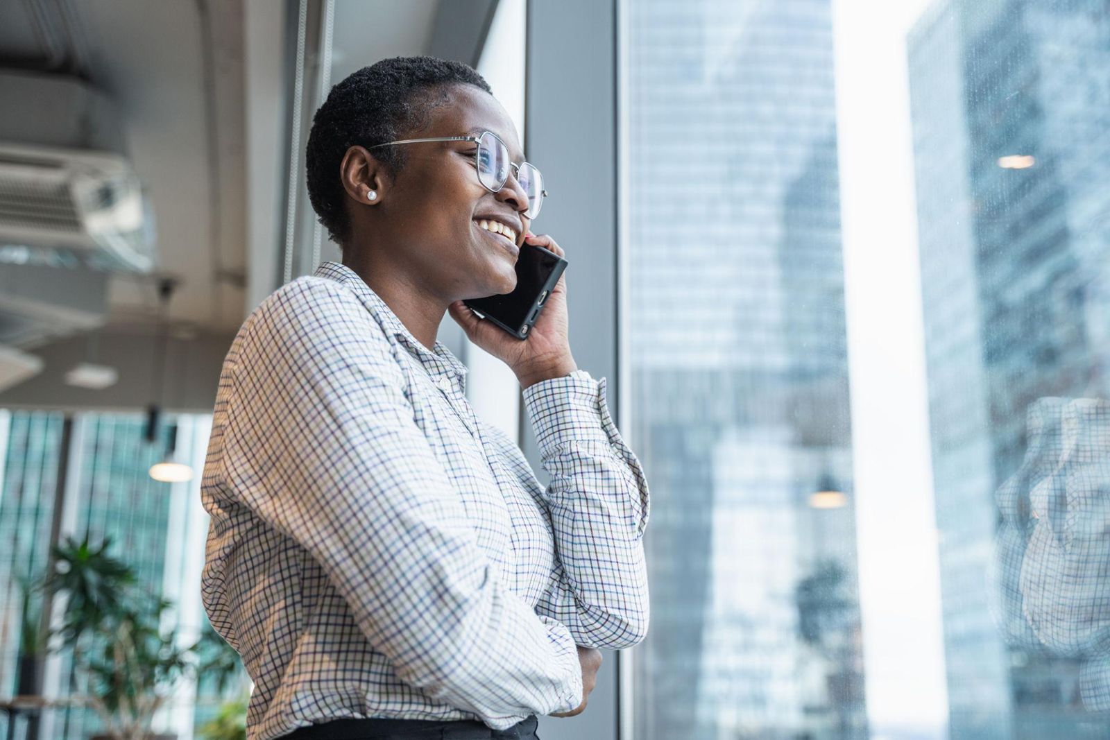 Iemand staat in een kantoor bij het raam, met de telefoon aan het oor, en lacht tijdens het gesprek